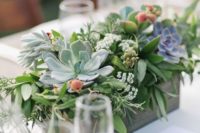 a fresh wedding centerpiece of a plywood planter, much greenery, succulents and berries and some wildflowers