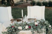 a greenery and blush and burgundy bloom table runner, a sign and some candles to mark the table