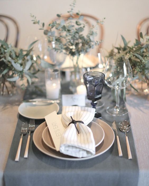 a grey and neutral wedding table with silver eucalyptus, candles, grey table runners, plates and glasses looks peaceful and stylish
