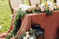 a large candle lantern, florals, a sign, a greenery and bloom table runner and candleholders for elegant decor