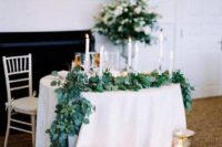 a lush greenery table runner, lots of candles and urns with candles for an elegant touch and to mark the table