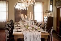 a luxurious vintage wedding reception space with crystal chandeliers, a lace table runner, pink blooms and tall and thin candles is adorable