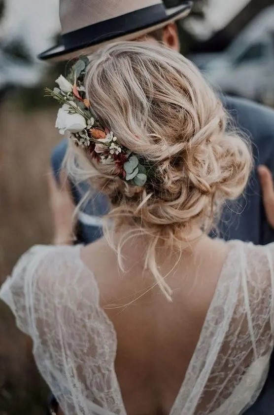 a messy and loose wedding low updo with waves and locks down and with a floral accent - neutral and blush blooms and greenery