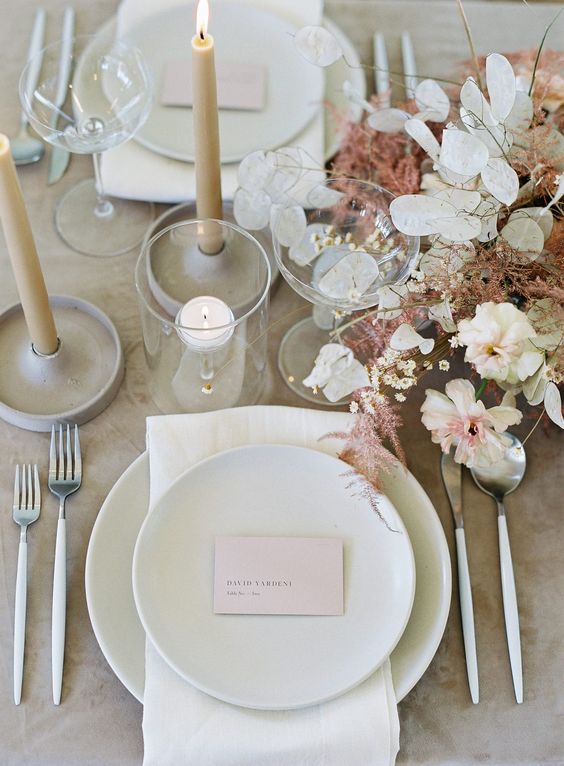 a modern and refined spring wedding tablescape with white porcelain and neutral linens, neutral and pink blooms and ivory candles