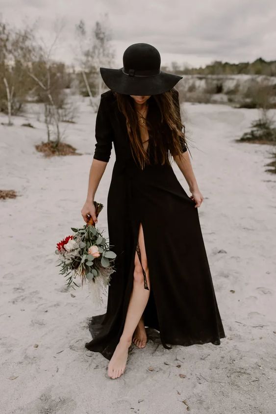 a modern black A-line wedding dress with a plunging neckline and a slit, short sleeves and a black hat is amazing for a modern wedding