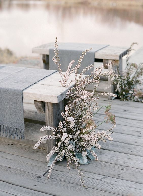 a natural wedding ceremony space with wooden benches covered with grey wool and neutral lush blooms