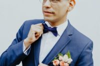 a navy suit, a navy bow tie and a coral and blush floral boutonniere for a whimsy and bright groom’s look