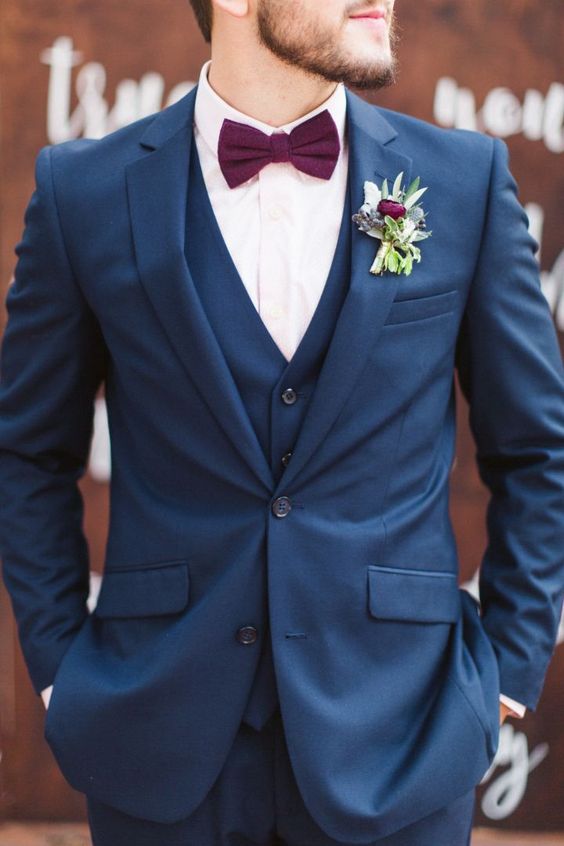 a navy three-piece suit, a blush shirt, a purple bow tie and a floral boutonniere for a bold summer or fall look