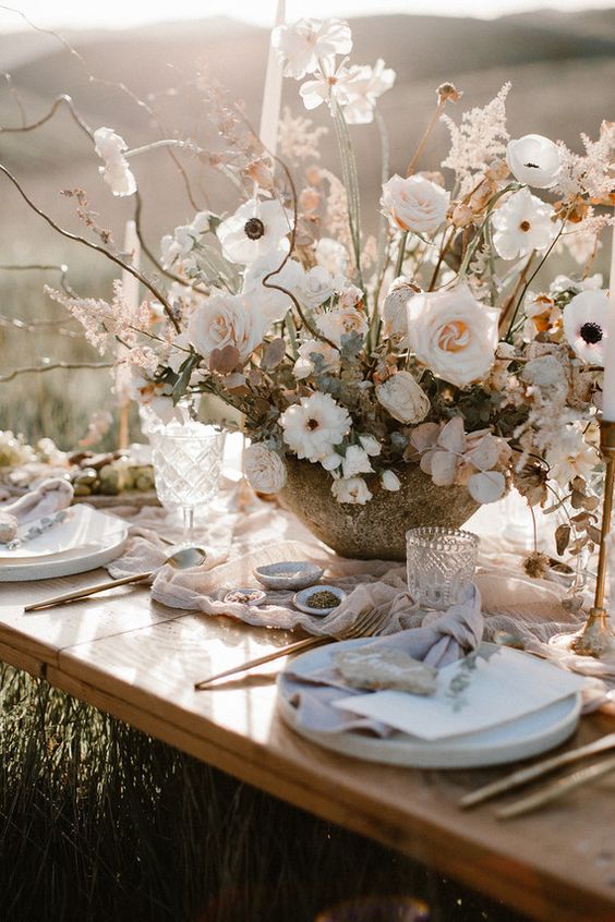 a neutral boho spring wedding tablescape with blush and white blooms, a blush runner, white plates and gold cutlery