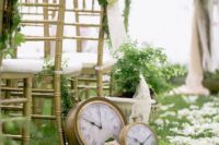 a refined wedding aisle decorated with white petals, pink blooms, greenery and large clocks looks chic