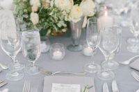 a romantic grey wedding table setting with a grey tablecloth, napkins, neutral blooms and lots of candles