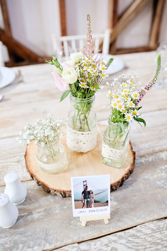 a rustic wedding centerpiece of a wood slice, jars wrapped with burlap and wildflowers plus a photo is a lovely idea for a wedding