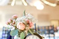 a rustic wedding centerpiece of pink and white blooms and greenery, candles and a large clock on a wood slice