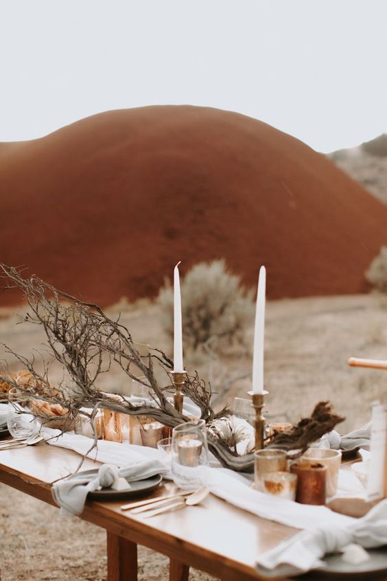 a safari wedding tablescape with a neutral runner, candles of various kinds, driftwood and black plates