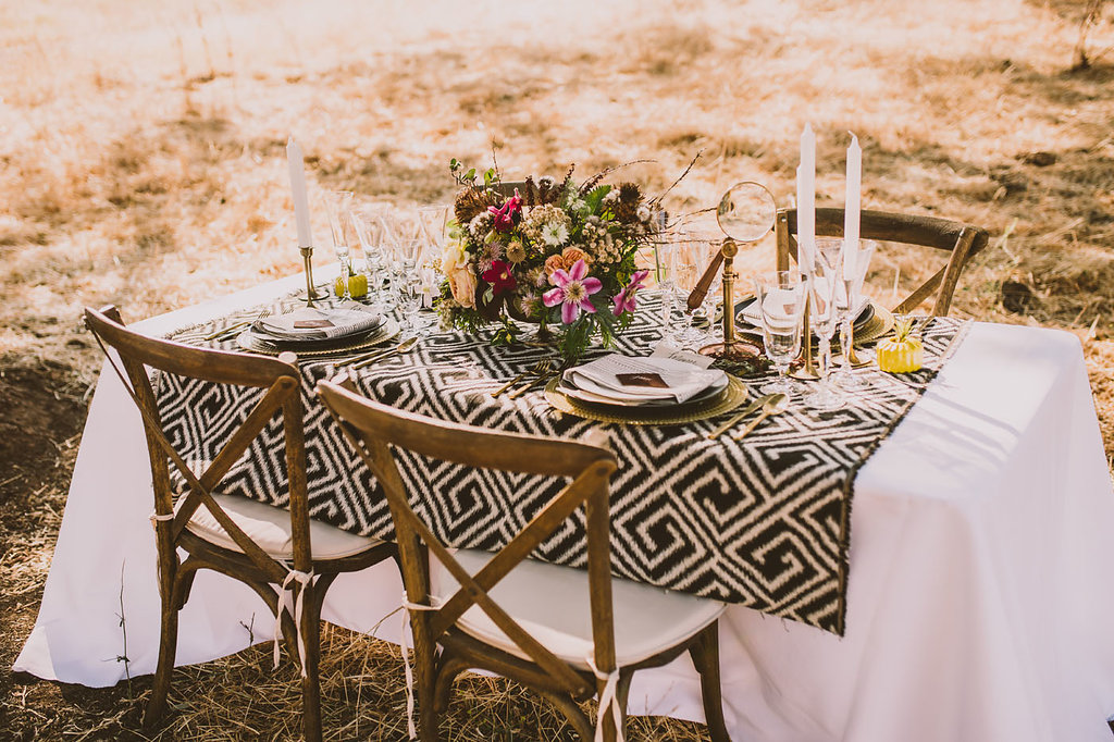 a safari wedding tablescape with a printed table runner, gold chargers, candleholders, bold blooms and greenery