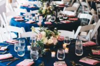 a simple and elegant wedding tablescape with a navy tablecloth, coral napkins, candles and ivory and coral blooms