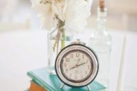 a sweet and airy wedding centerpiece of a stack of books, candles, white blooms and a vintage clock on top