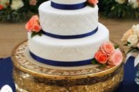 a textural white wedding cake with navy ribbons and coral and blush blooms for decor