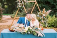 a triangle wedding arch with lush greenery, florals can be a nice accent for the sweetheart table