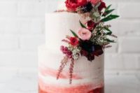a watercolor wedding cake in pink and red, with burgundy, pink and red blooms and greenery