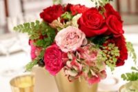 a wedding centerpiece of a gold bucket, pink and red blooms, greenery and candles plus some green hydrangeas
