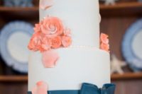 a white wedding cake decorated with coral sugar blooms and petals, a navy ribbon and a romantic cake topper