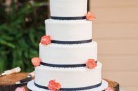 a white wedding cake with navy ribbons, coral blooms and a monogram boutonniere is timeless classics