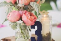 a wooden slice, a navy yarn covered table number, a candle in a jar and corla pink blooms in jars as a cool rustic centerpiece