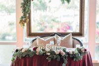 an empty frame with greenery and blush and burgundy blooms, a matching table runner and candle lanterns