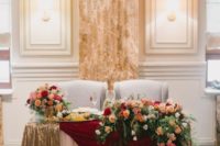 elegant gold and burgundy tablecloths, lush florals and greenery and a glass bowl with fruits