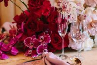 lush table decor with hot pink, red and light pink blooms and pink napkins plus gold cutlery for a luxurious wedding