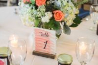 navy napkins, a coral pink table number, a bright floral centerpiece of white, blue and coral blooms for a table setting at the reception