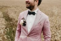 tan pants, a pink blazer, a polka dot black bow tie and a floral boutonniere for a chic summer groom’s outfit