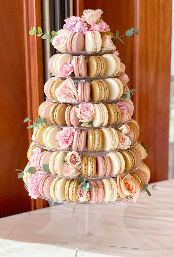 a beautiful clear stand with various pastel macarons and pastel blooms and greenery for a delicate and romantic wedding