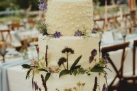a boho wildflower wedding cake with lots of pressed edible blooms and leaves and polka dots on top