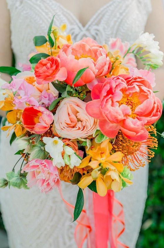 a bold wedding bouquet with red, pink, blush and yellow blooms, some greenery and coral ribbons for a bolder look
