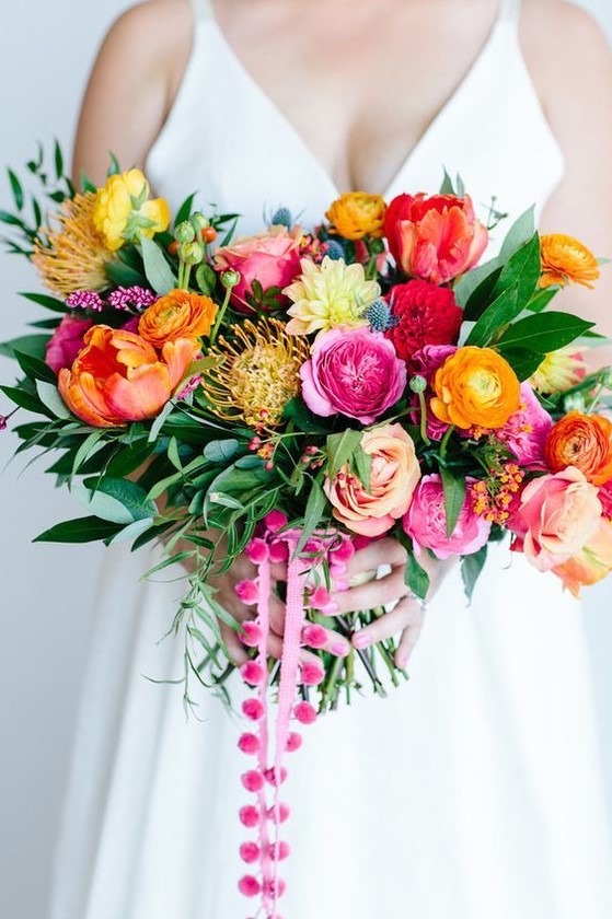 a bold wedding bouquet with yellow, orange, pink, blush, yellow blooms, pincushion proteas, greenery and pink pompoms