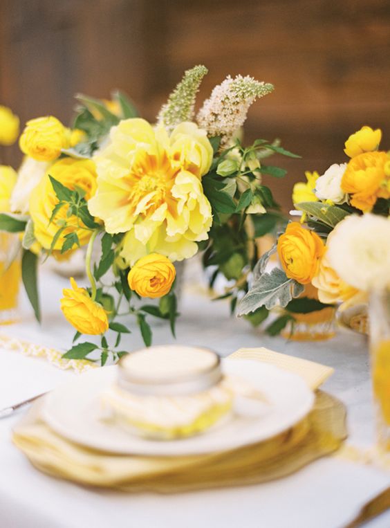 a bright and chic wedding table setting with yellow blooms and greenery, yellow plates and a favor in a jar