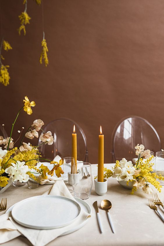 a charming spring wedding tablescape with neutral linens, yellow and white blooms, mustard candles, white and gold cutlery