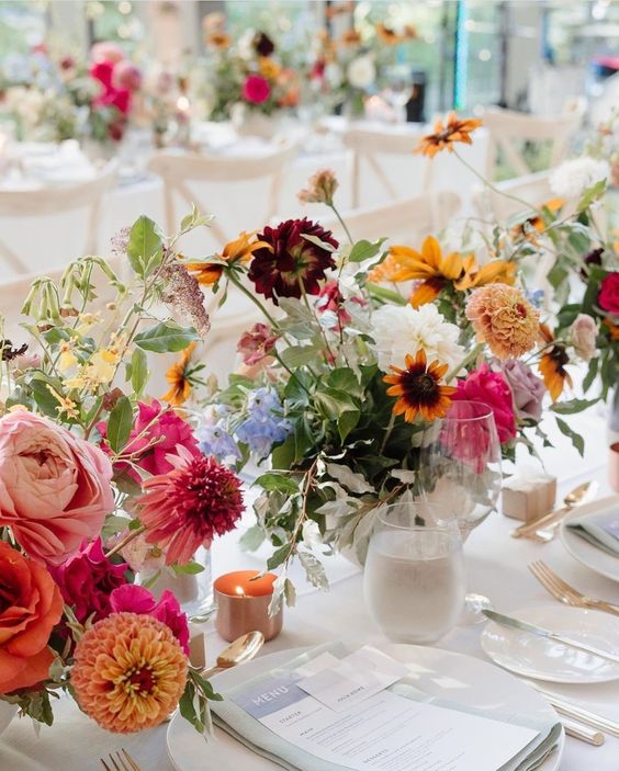 a chic neutral wedding tablescape accented with colorful floral centerpieces and candles, with neutral stationery