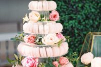 a clear multi-tier stand with lots of blush macarons serve, with blush and pink blooms and greenery is a gorgeous idea for a wedding