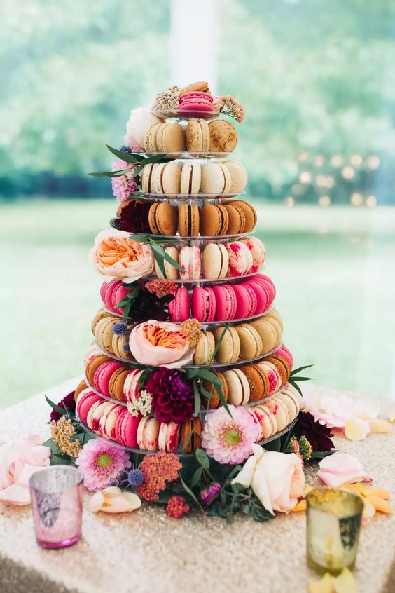 a clear stand with colorful macarons, bright and pastel blooms and greenery is a cool solution for a bright wedding and a nice alternative to a usual wedding cake