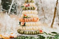a clear stand with neutral, green and coral macarons and greenery and berries is a beautiful alternative to a usual wedding cake