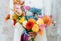 a gorgeous bright wedding bouquet that includes neutral, blue, red, pink, purple glowers and colorful ribbons