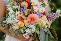 a hoppy summer wildflower wedding bouquet done in purple, white, yellow, orange and pink, with greenery and seed pods