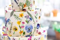 a lovely colorful wedding cake with lots of bright pressed flowers and leaves for a bright summer wedding