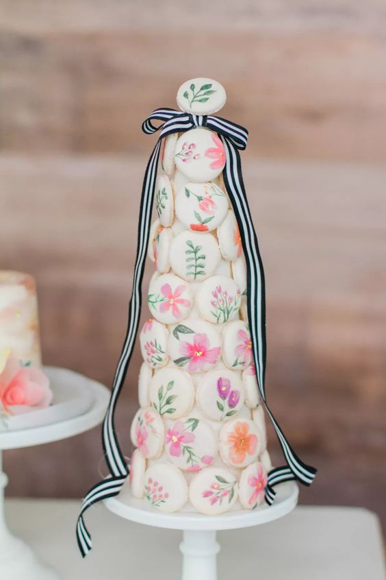 a macaron tower made of floral painted macarons and with a striped bow with long ribbons for a refined and romantic wedding
