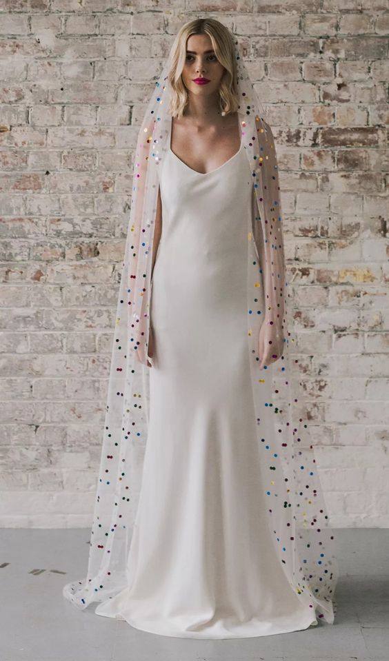 a minimalist wedding dress with a white veil dotted with colorful polka dots are an amazing and bold combo