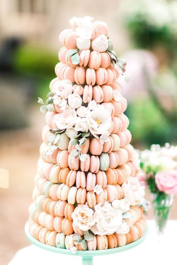 a mint stand with a large macaron tower composed of pink and green macarons, with greenery and white blooms for a pastel wedding