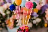a naked wedding cake with berries and blooms, with colorful pompoms on sticks is a lovely idea for a cheerful party wedding
